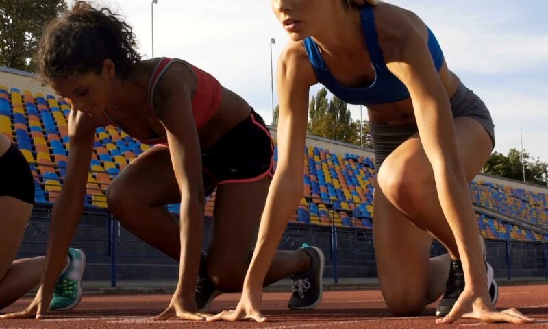 prikaz dve devojke koje se bave atletikom na stazi za trčanje u čučećem položaju pre trčanja