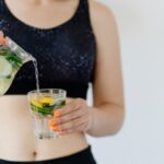 Žena u sportskoj opremi sipa vodu sa limunom i krastavcem u čašu kao deo detoksa organizma za jedan dan