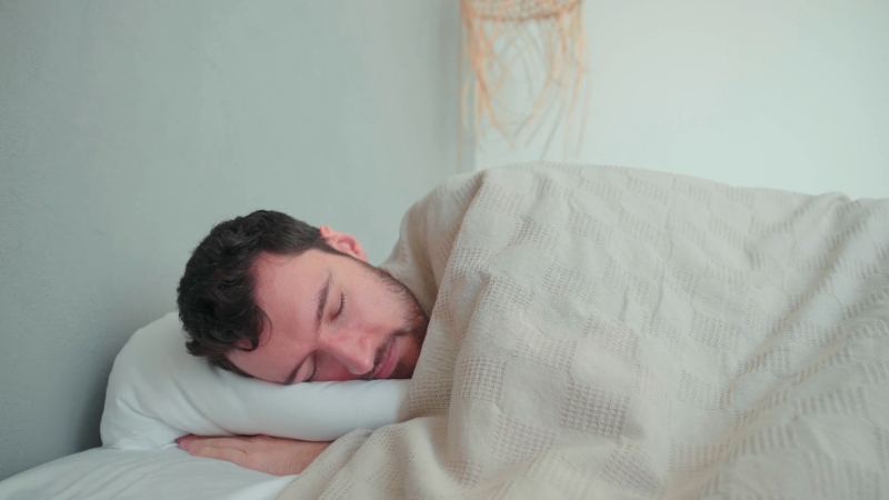 Čovek pokriven ćebetom, spava na boku u krevetu